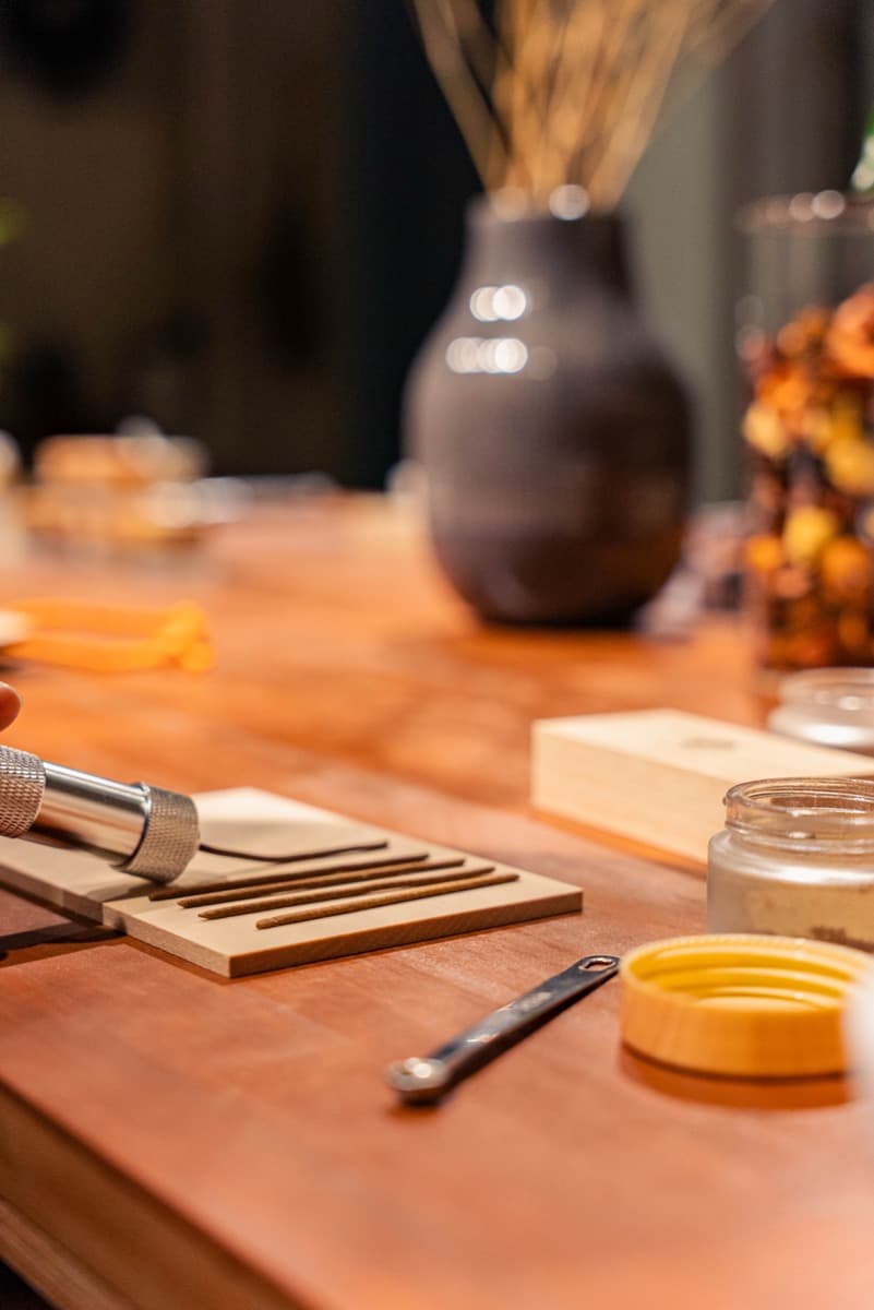 Finished incense sticks lined up on a wooden tray, with fragrance jars